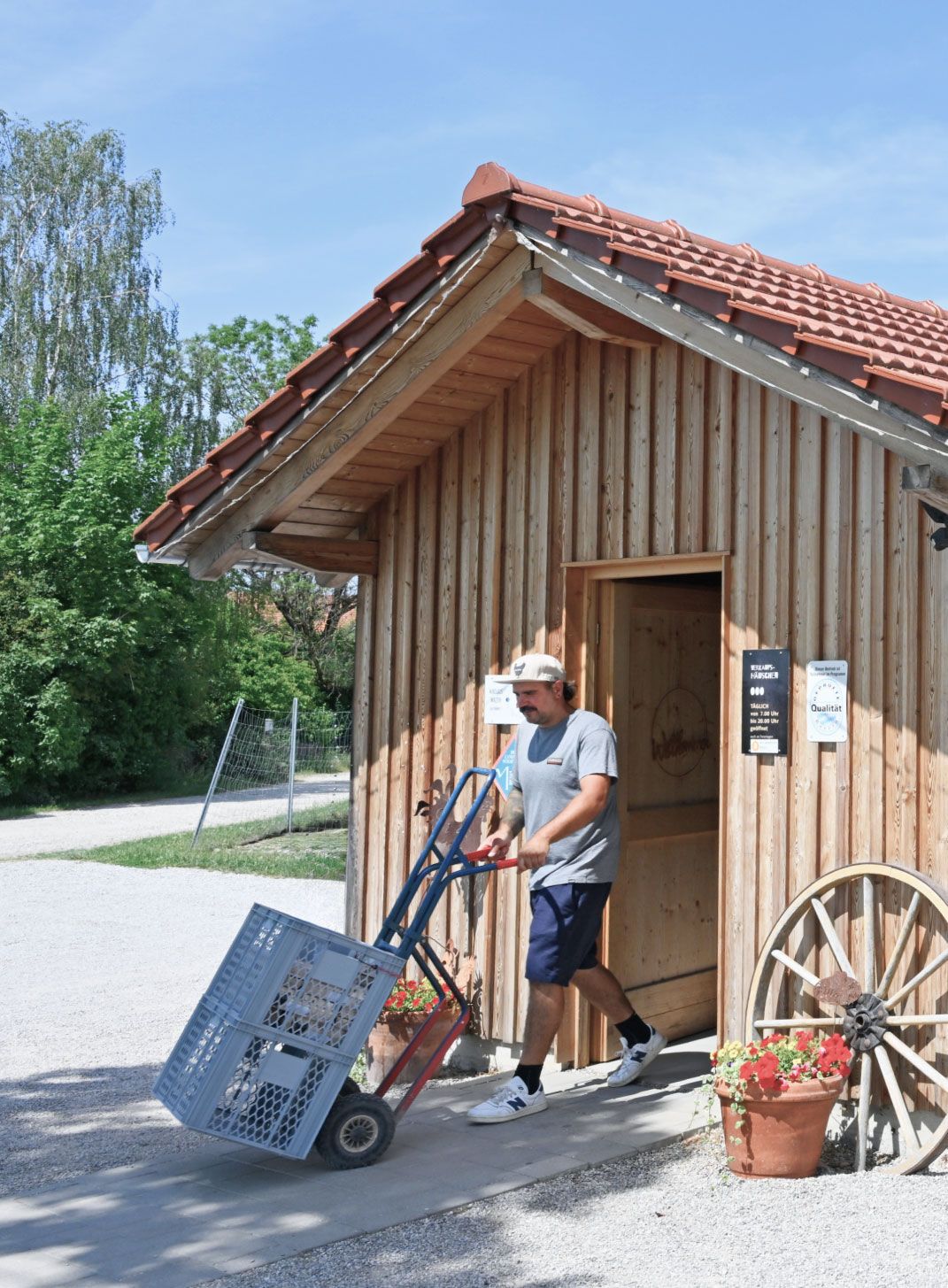 Nikolaus Walter, Landwirt von Gut Hollern und regionaler Lieferant des Flughafens München, transportiert mit einer Sackkarre Klappkisten vor einem hölzernen Verkaufshäuschen.